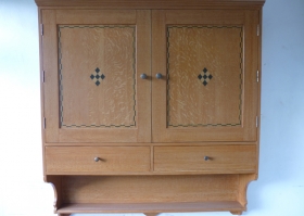 A wall-mounted TV cabinet influenced by the Arts and Crafts movement in simulated oak and inlay. Wall Mounted TV Cabinet